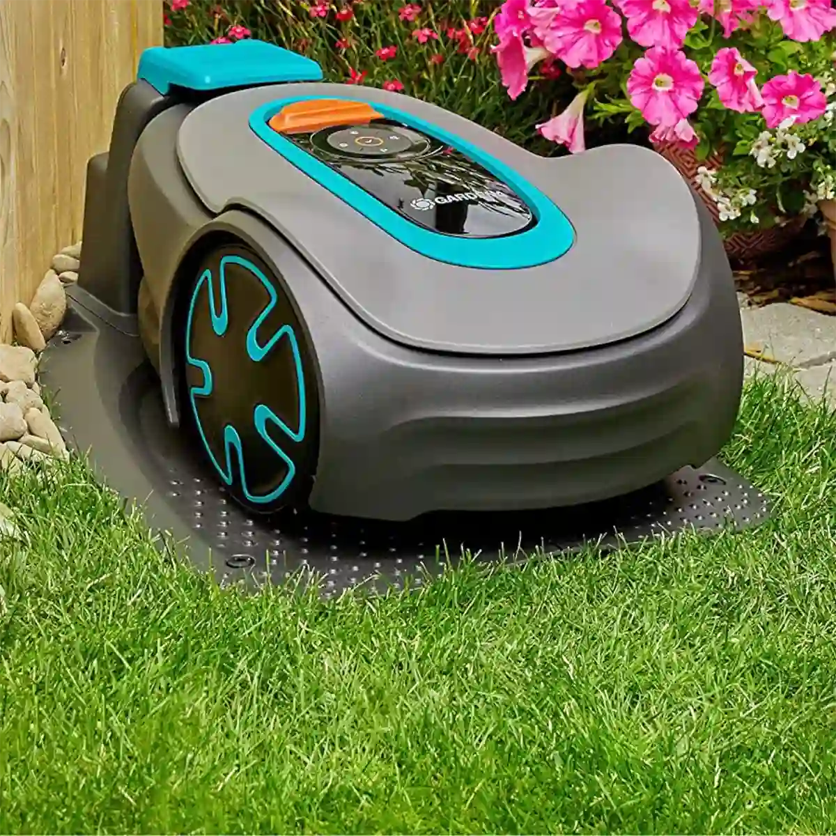 Der GARDENA 15202-20 SILENO minimo Mähroboter dockt auf dem Rasen an einem Holzzaun und rosa Blumen an und bietet innovative Rasenpflege mit smarter Bluetooth-App-Steuerung.
