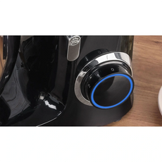 Eine Nahaufnahme der MPM MRK-19 Planeten-Küchenmaschine von MPM mit schwarzem Finish, silbernem und schwarzem, auf Null gestelltem Drehknopf mit blauem LED-Ring, weißer Nummerierung und einem leistungsstarken 2200-Watt-Motor auf einer Holzoberfläche.