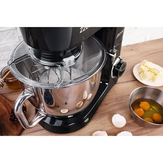 Eine MPM MRK-19 Planeten-Küchenmaschine mit 2200 Watt und Metallschüssel steht auf einer Holztheke. Aufgeschlagene Eier, Schalen, Butterwürfel und der Schneebesen mit planetarischem Rührsystem stehen in der Nähe zum Backen bereit.