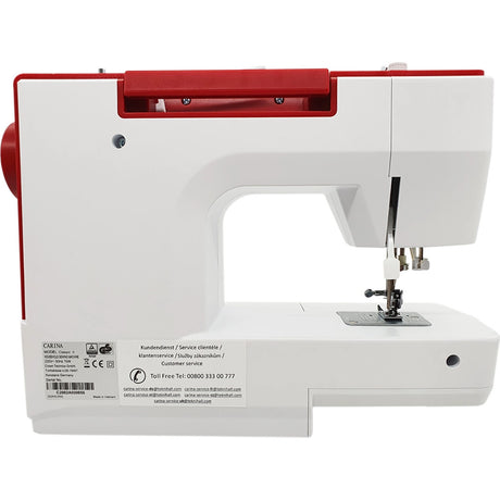 Eine weiß-rote CARINA Classic II Freiarm-Nähmaschine von CARINA wird von der Seite gezeigt, wobei der Nadelbereich, der Nähfuß, der Spulenstift und die Bedienknöpfe hervorgehoben werden. Auf der unteren linken Seite der Maschine sind Aufkleber und Serviceinformationen zu sehen.