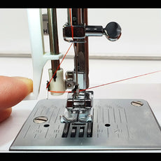 Nahaufnahme einer Nähmaschinennadel beim Einfädeln, wobei ein Finger den Faden führt - ein Beispiel für die Präzision und Leichtigkeit der CARINA Classic II von CARINA.