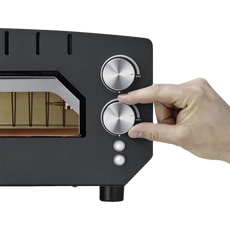 Eine Hand dreht den Drehknopf am schwarzen CASO 2249 PizzaChef 400° Pizza-Ofen mit zwei silbernen Drehreglern für Ober-/Unterhitze und Kontrollleuchten.