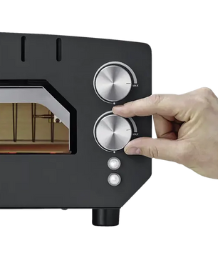 Eine Hand dreht den Drehknopf am schwarzen CASO 2249 PizzaChef 400° Pizza-Ofen mit zwei silbernen Drehreglern für Ober-/Unterhitze und Kontrollleuchten.