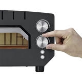 Eine Hand dreht den Drehknopf am schwarzen CASO 2249 PizzaChef 400° Pizza-Ofen mit zwei silbernen Drehreglern für Ober-/Unterhitze und Kontrollleuchten.