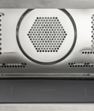 Nahaufnahme der CASO HCMG 25 Mikrowelle - silber interior: 25-Liter-Garraum aus Edelstahl mit sechseckigen Lüftungsschlitzen und Perforationen für die Luftzirkulation, ideal für eine verbesserte Heißluftfunktion. Die Backofentür ist unten teilweise geöffnet. Marke: CASO.