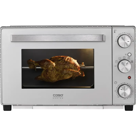 Ein ganzes Brathähnchen auf einem Grill mit Drehspieß im CASO TO 32 SilverStyle Mini-Backofen von CASO (silber) mit Drehreglern und Umluftfunktion.