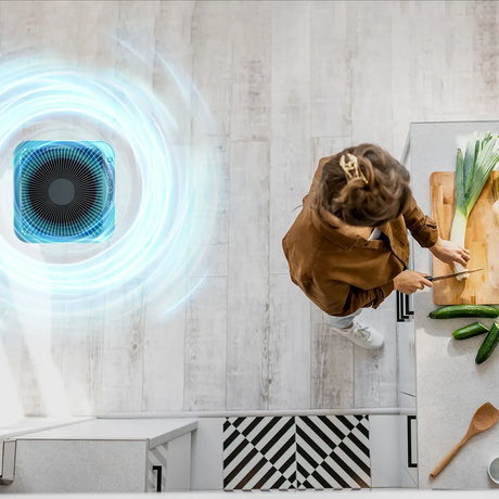 Draufsicht auf eine Frau beim Gemüseschneiden in der Küche mit dem Genius INVICTUS Air P7 Luftreiniger - Grau von INVICTUS, der mit einem leistungsstarken HEPA-13-Filter ausgestattet ist und saubere Luft in die Nähe bläst.