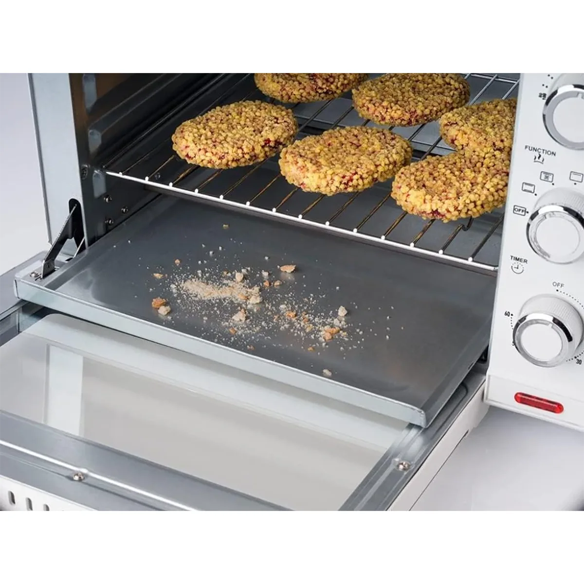 Eine Nahaufnahme des Korona 57158 Multifunktions-Toastofens - silber zeigt das Backen von Keksen auf einem Rost, Krümel auf dem ausziehbaren Tablett und die Bedienelemente auf der rechten Seite. Dieser 24-Liter-Ofen von Korona ist perfekt für jede Küche.