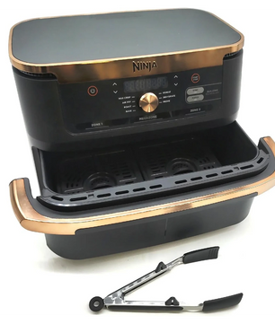 Eine schwarz-goldene Ninja Foodi FlexDrawer Dual Zone Heißluftfritteuse von Ninja mit zwei 4-Liter-Körben wird mit einer Metall-Küchenzange davor gezeigt.