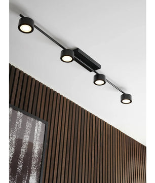 Die Nordlux Clyde Deckenleuchte in schwarz von Nordlux verfügt über vier verstellbare runde Strahler im skandinavischen Design, die sich ideal für die Montage über vertikalen Holzlatten und einem schwarz gerahmten abstrakten Kunstwerk eignen.