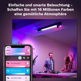 Die Philips Hue Centris 4-flammig - Schwarz von Philips leuchtet blau und rosa in einem modernen Wohnzimmer, während sich zwei Personen an einem Tisch unterhalten. Eine Smartphone-App steuert das Licht mit deutschem Text, der die Funktionen der intelligenten Beleuchtung erklärt.