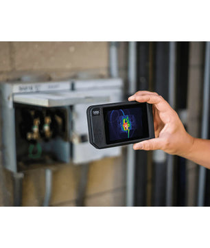 Hand hält eine Seek Thermal SHOT PRO Wärmebildkamera - schwarz von Seek Thermal, beim Scannen eines auf einer Ziegelwand montierten Elektroschranks.