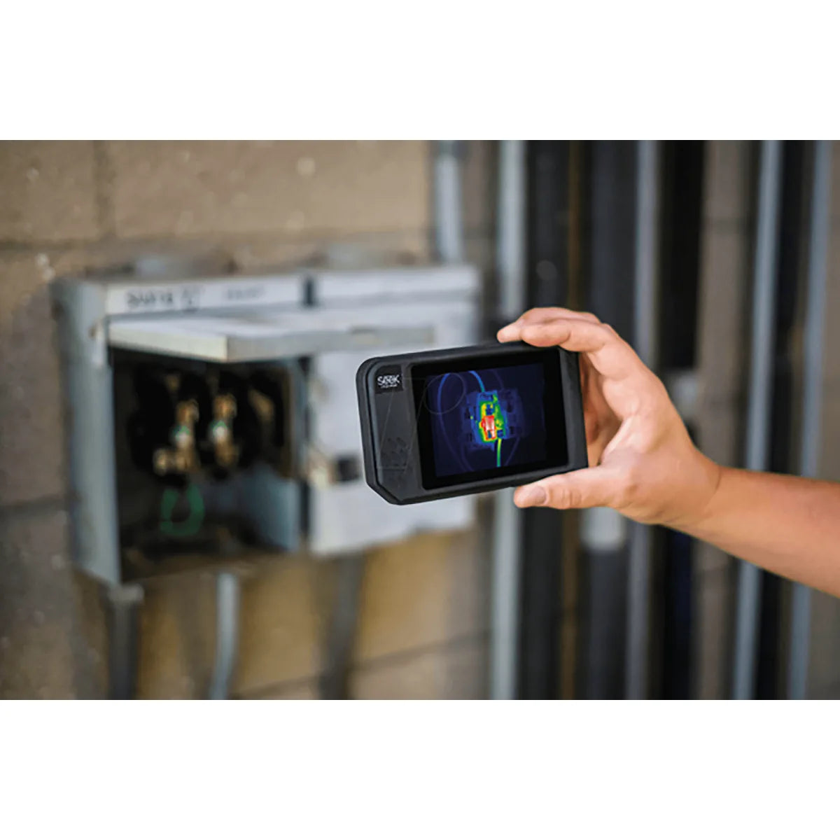 Hand hält eine Seek Thermal SHOT PRO Wärmebildkamera - schwarz von Seek Thermal, beim Scannen eines auf einer Ziegelwand montierten Elektroschranks.