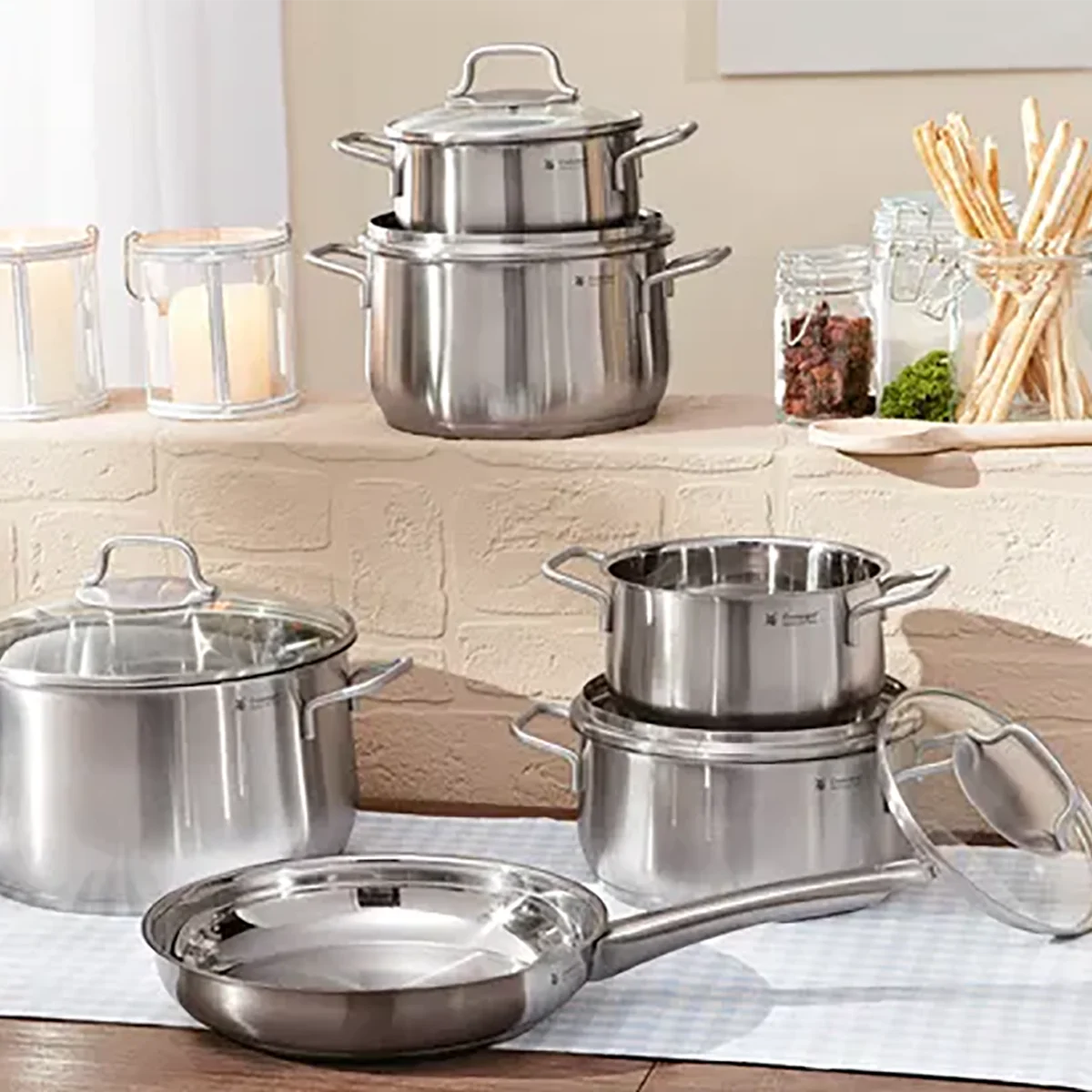 Das 6-teilige WMF Brillant Kochgeschirr-Set aus Edelstahl mit Glasdeckeln steht auf Tisch und Arbeitsplatte - spülmaschinengeeignet, induktionsgeeignet und ideal für moderne Küchen.