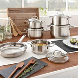 Das WMF Brillant Kochgeschirr-Set 6-teilig aus Edelstahl steht spülmaschinengeeignet mit Töpfen, Pfannen und Deckeln auf der Küchentheke neben Kräutern und einer Avocado, die an ein Fenster mit Blick ins Grüne grenzt.